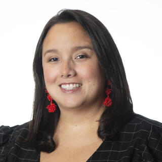 Dark haired woman, smiling, wearing red earrings and a black and white blouse
