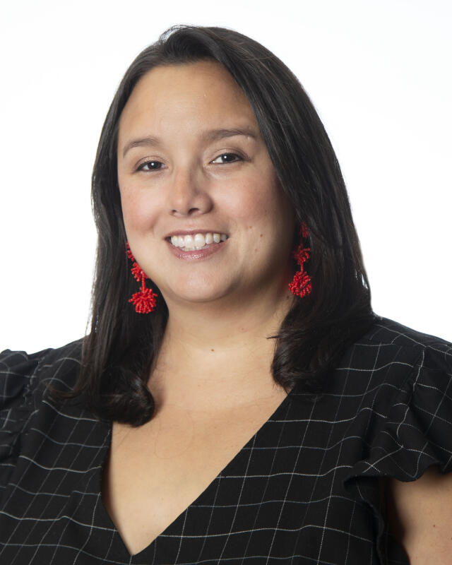 Dark haired woman, smiling, wearing red earrings and a black and white blouse
